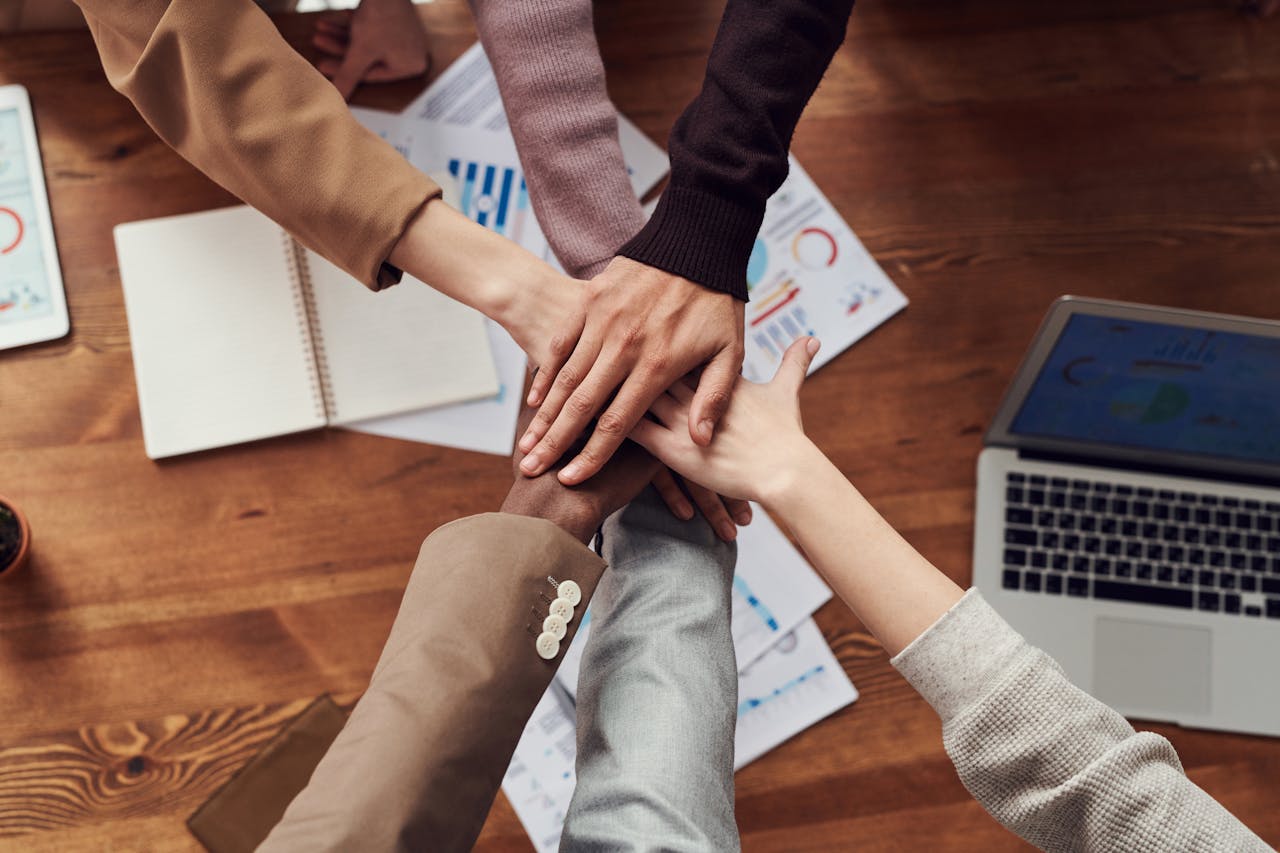 Diverse professionals unite for teamwork around a wooden table with laptops and documents.