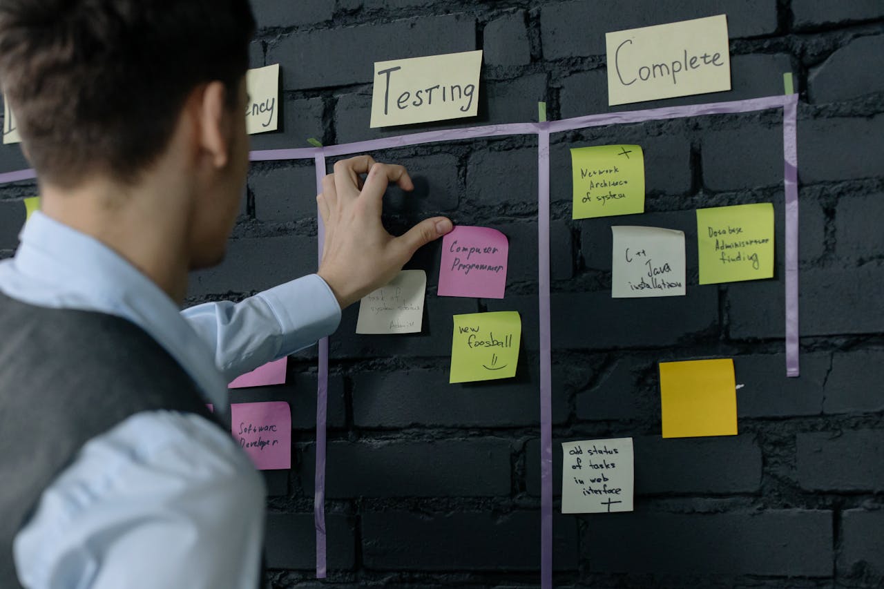 Man organizing project tasks on a wall using sticky notes in a modern office setting.